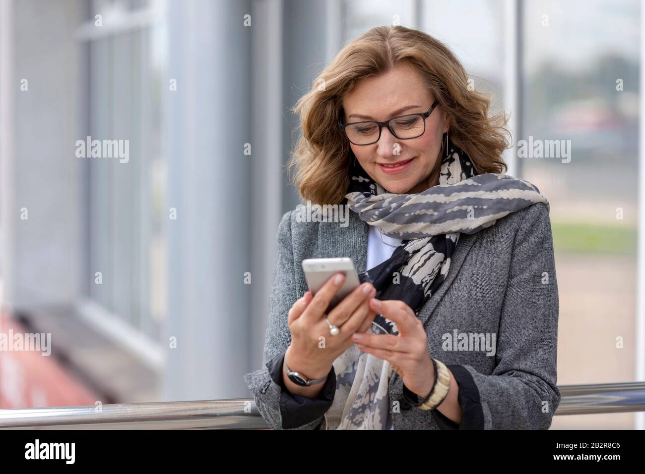 Portrait d'une femme d'affaires souriante dans des lunettes regardant le téléphone mobile. Belle femme mûre à l'extérieur Banque D'Images