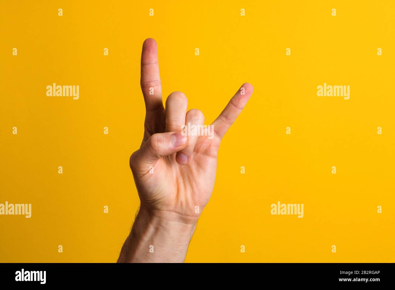 rock it. main d'homme montrant le geste de signe de rock sur un fond jaune avec une ombre dramatique Banque D'Images