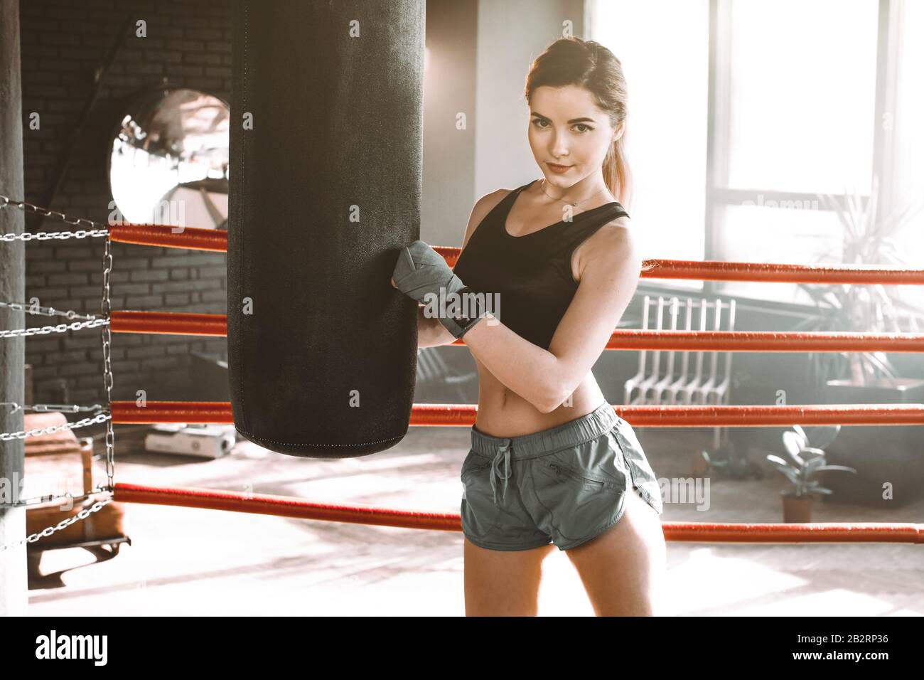 Entrainement de boxeur feminin a l interieur d un anneau de boxe. Boxer pratiquant ses mouvements dans un studio de boxe. La jeune fille tape un sac de poinconnement et regarde l appareil photo Photo