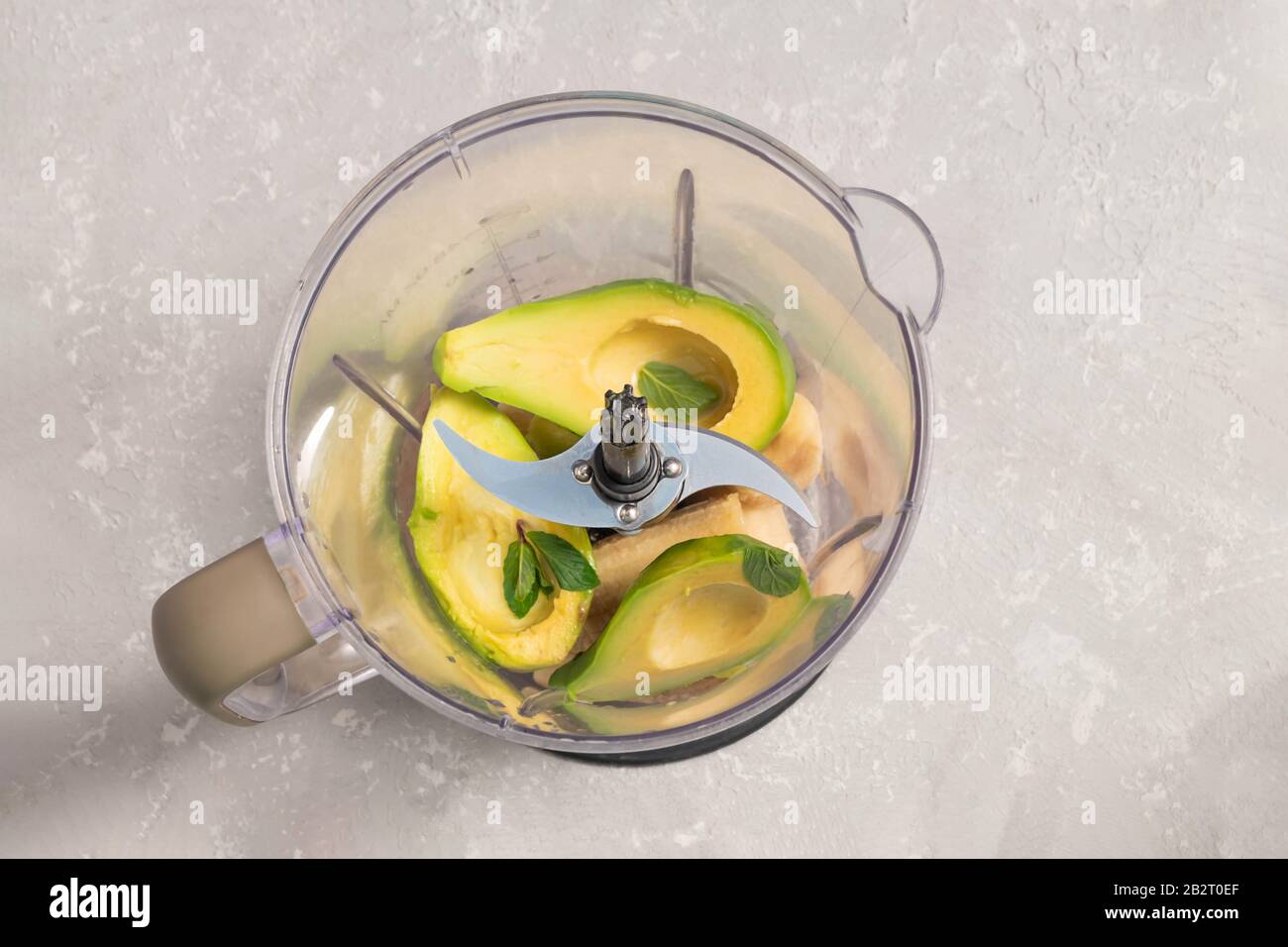 Blender avec avocat, feuilles de banane et de menthe congelées pour crème glacée avocat sur fond gris neutre, vue de dessus Banque D'Images