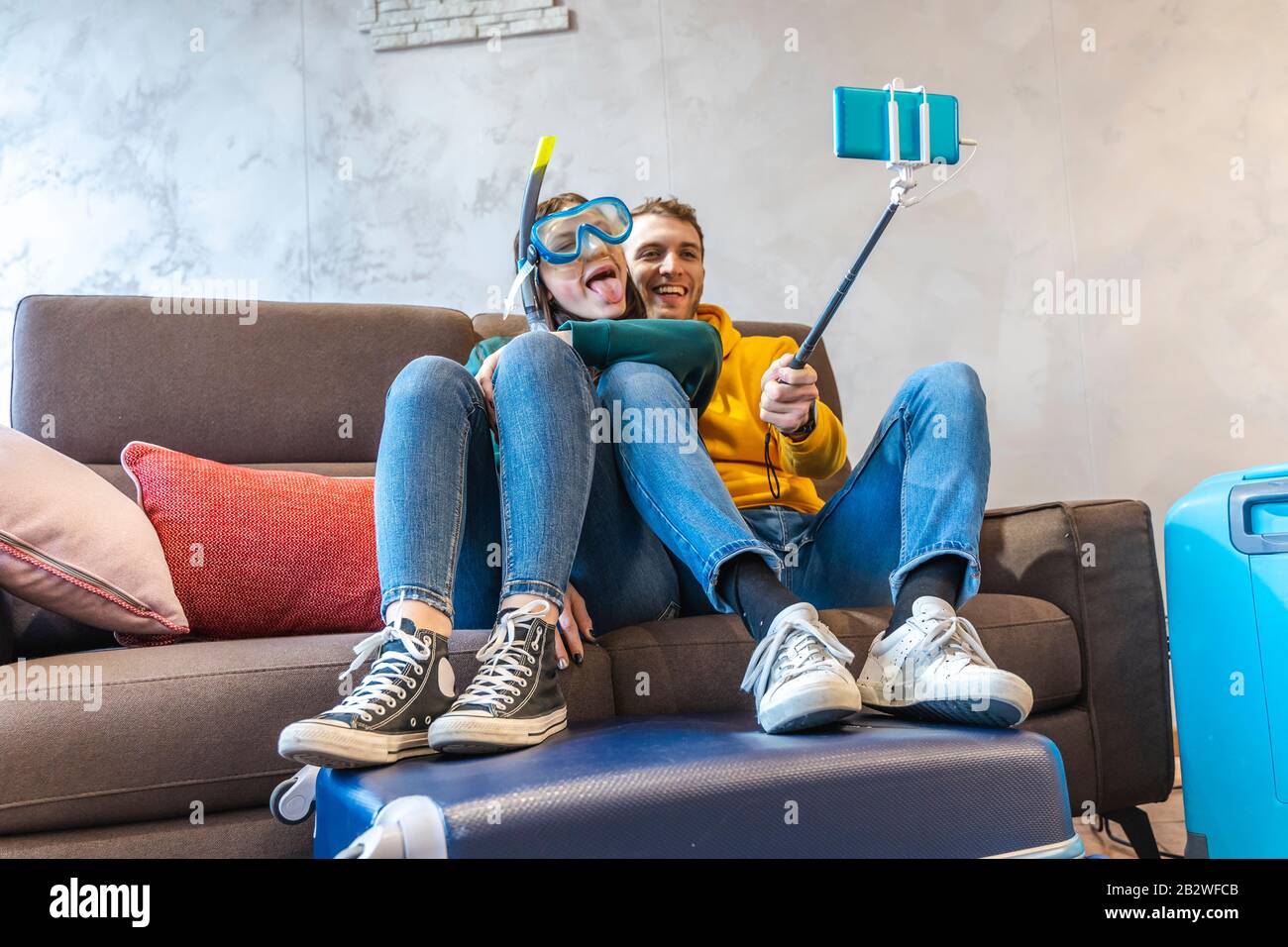 un jeune couple assis sur le canapé à la maison prend un selfie avec smartphone portant un masque de plongée avant de partir pour les vacances Banque D'Images