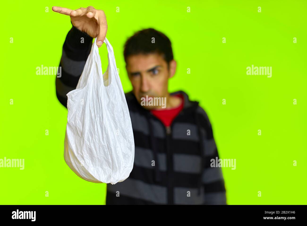 Un homme avec dégouste tient un sac en plastique devant un fond vert Banque D'Images