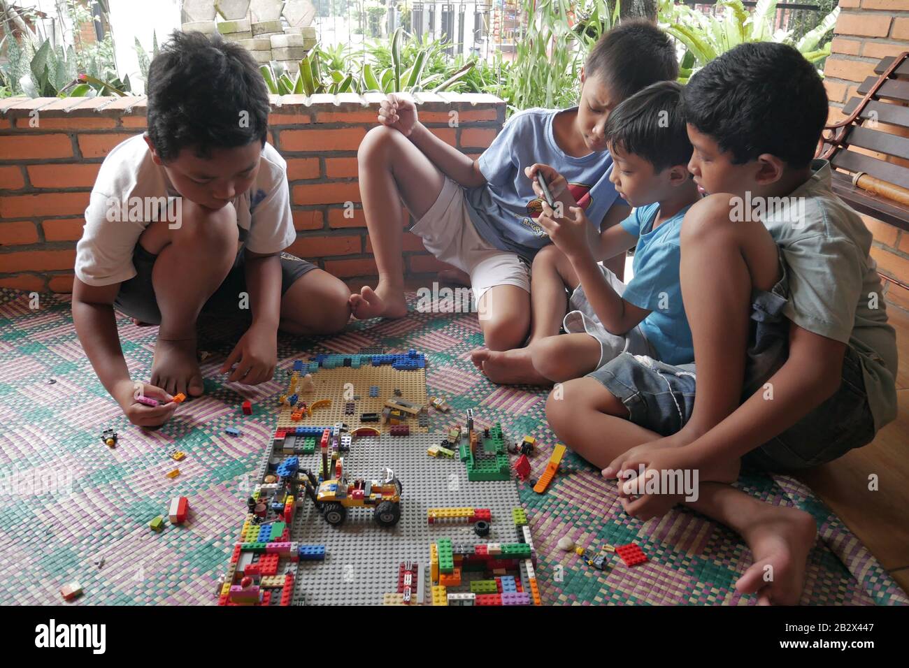 Un groupe d'enfants jouent au jouet Lego alors que l'un d'eux joue au jeu sur un smartphone. Banque D'Images