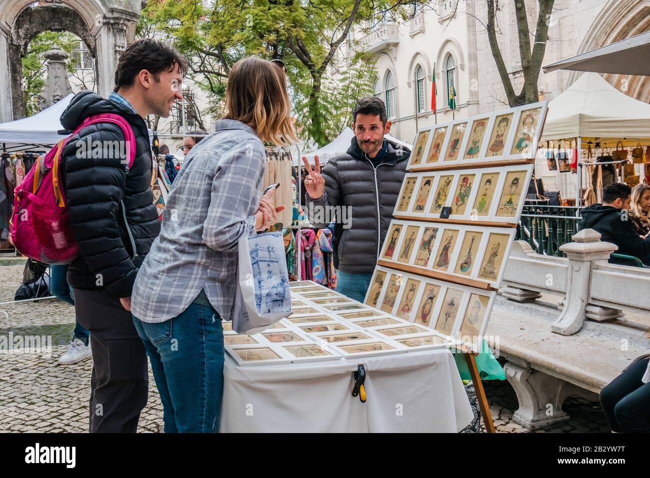 Un vendeur de rue de sexe masculin qui tente de vendre de l'art à un couple touristique à Lisbonne au Portugal pendant la saison de congé d'hiver Banque D'Images
