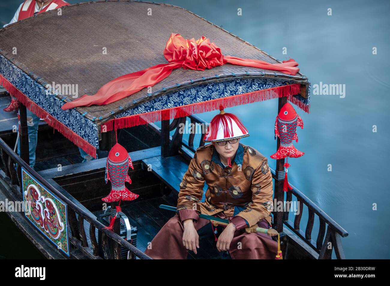 Wuxi, Chine - octobre 2019: Homme vêtu d'un costume chinois traditionnel sur une barge de rivière décorée, sur fond bleu. Banque D'Images
