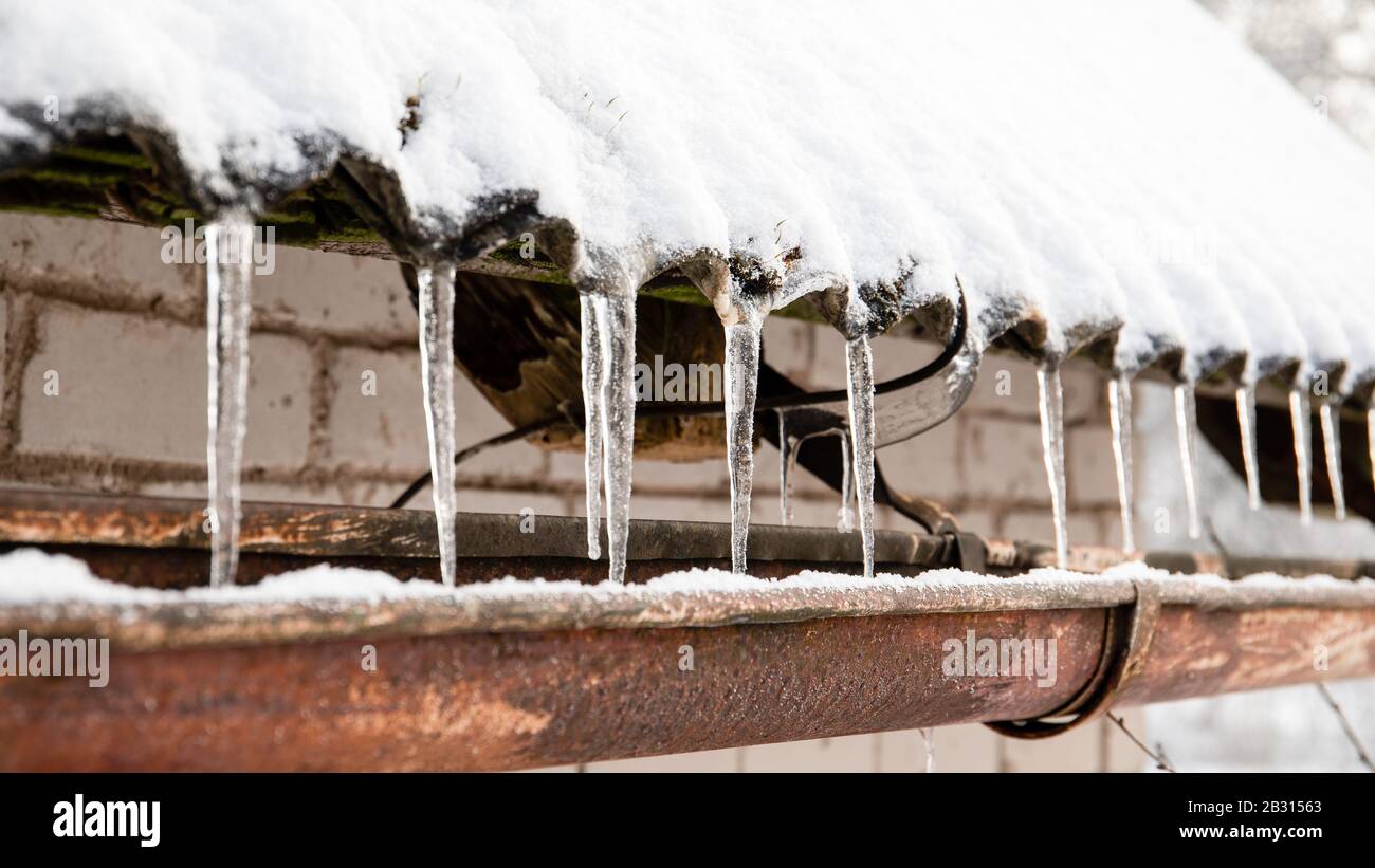 Des glaçons pendent du bord d'un toit. Dégel, fluctuations de température et arrivée du ressort Banque D'Images