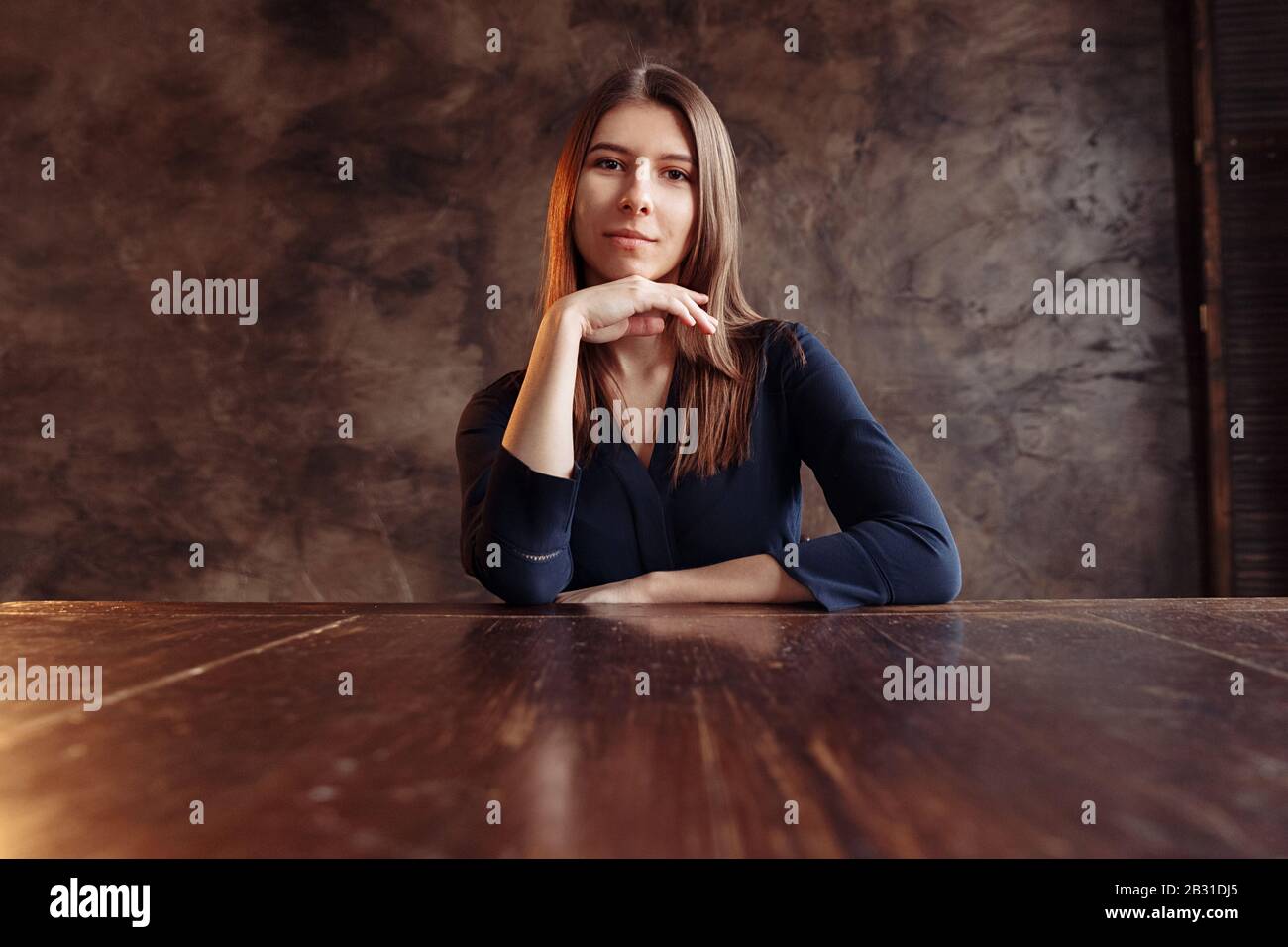 Une fille dans une chemise bleu foncé sibits à une table en bois. La main de fille soutient le menton. Banque D'Images