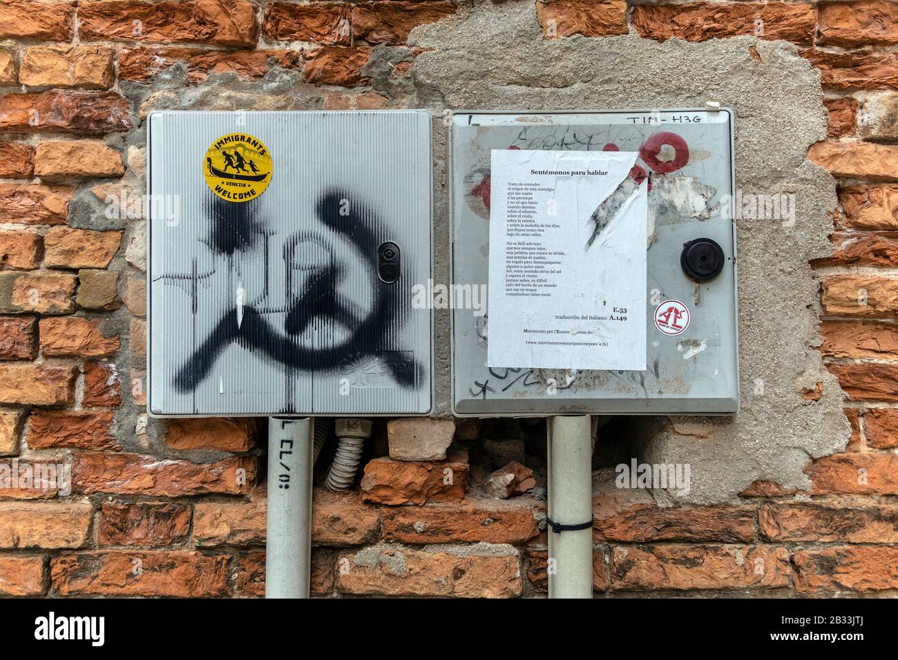 Graffitis sur les murs de la rue, Venise, Italie. Les immigrants accueillent l'autocollant et le marteau et la faucille Banque D'Images