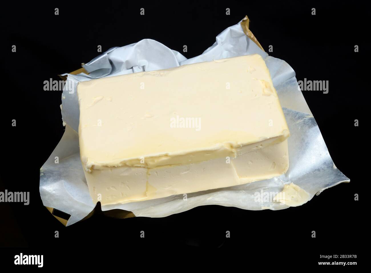 Margarine crémeuse dans un emballage industriel en feuille ouverte. Isolé sur prise de vue macro studio noire Banque D'Images