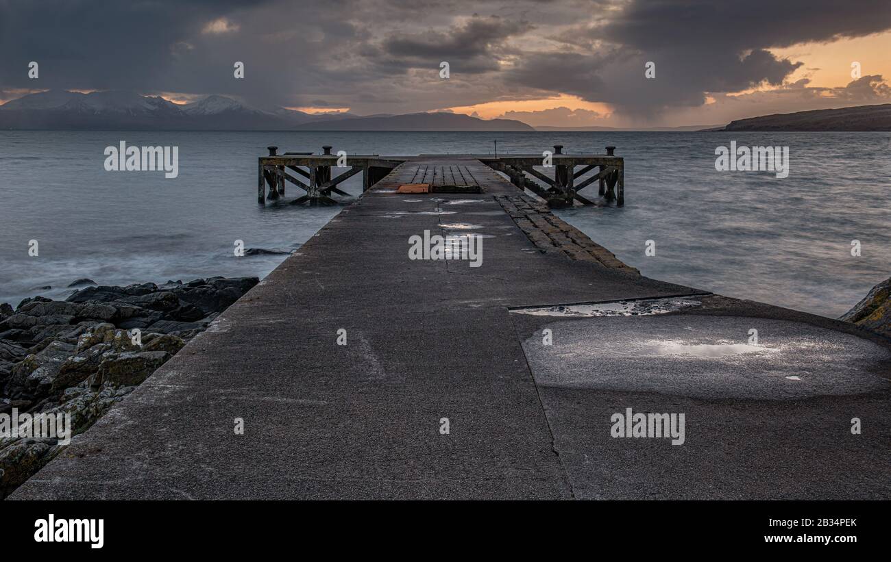 La vieille jetée de Portencross en Ecosse et les collines d'hiver sur l'île d'Arran tout comme le soleil descend produisant un spectaculaire coucher de soleil ciel. Banque D'Images