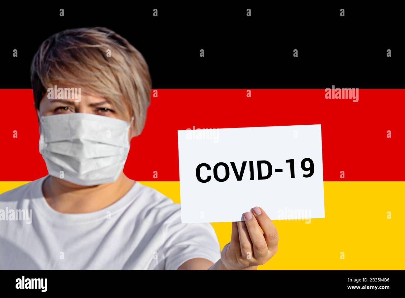 Femme dans le masque de visage tenir la feuille avec l'inscription Covid-19 contre le drapeau allemand. Concept d'attention sur la propagation du virus chinois De La Pneumonie à Coronavirus COVID-19 Novel Coronavirus dans le monde entier Banque D'Images
