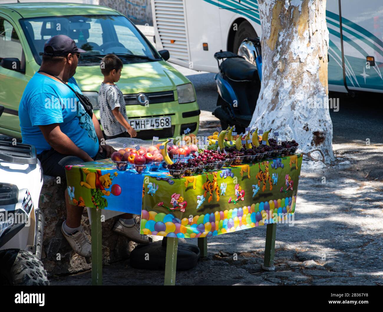 Fira, Grèce - 19 juillet 2019: Un vendeur de fruits avec un stand coloré juste à côté de la gare routière centrale de Fira au large de la rue Mirtropoleos Banque D'Images