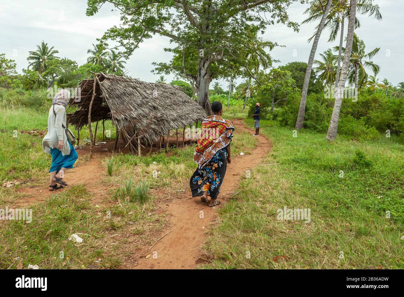 Deux femmes (une touriste et une femme locale) en longues robes marchant dans un village au Kenya Banque D'Images