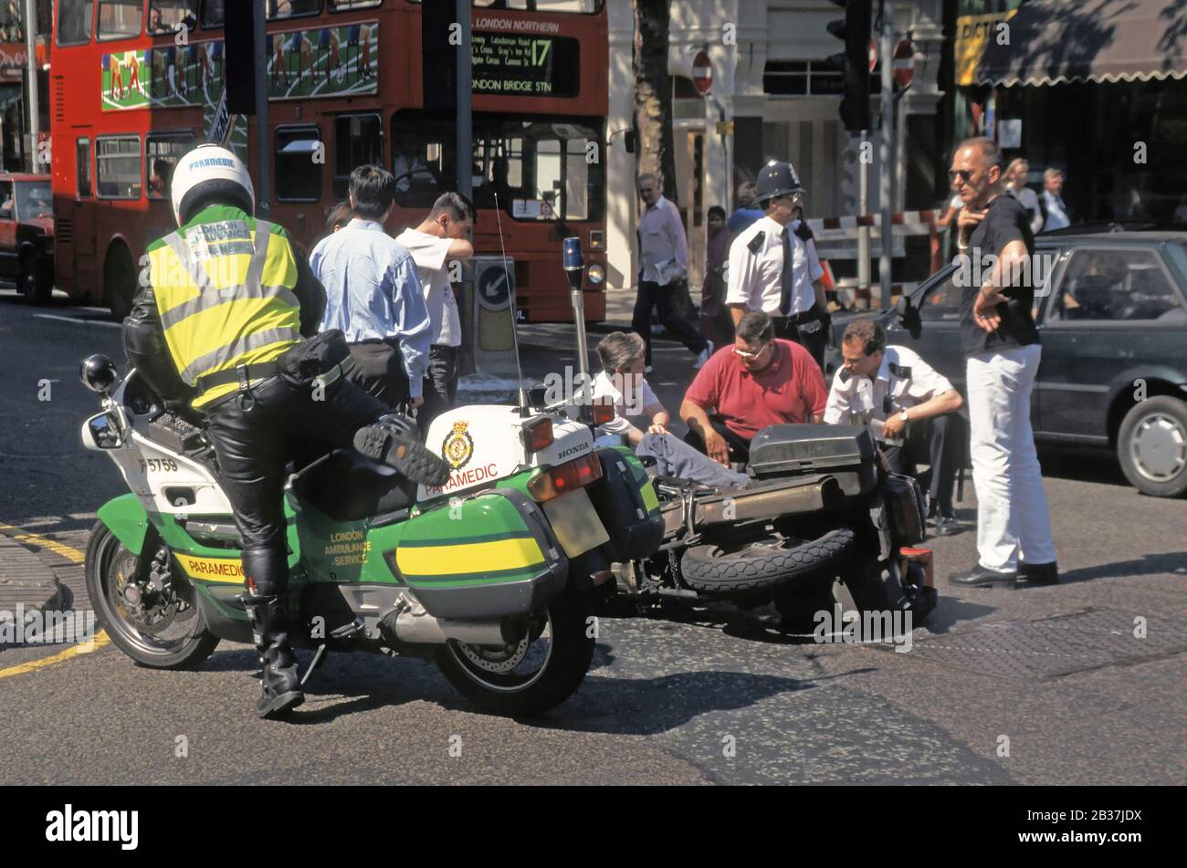 Le service ambulancier de Londres arrive en moto paramédical pour aider le  coursier de moto couché dans la route accident de la route scène de rue  Londres Angleterre Royaume-Uni Photo Stock -
