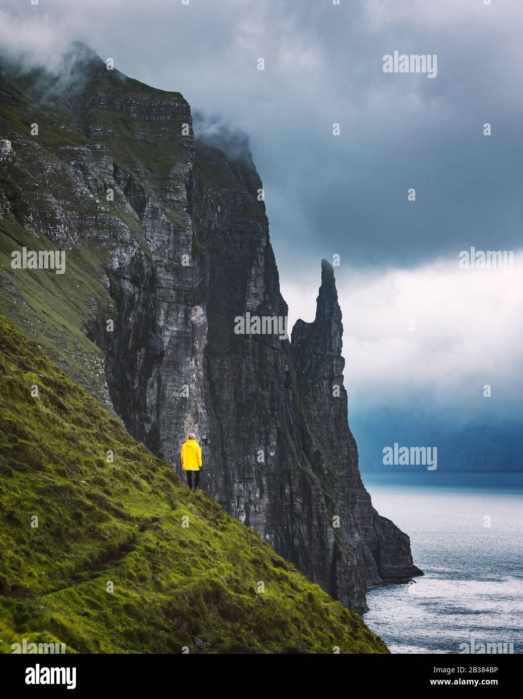 Touriste à yellow jacket porte sur les falaises d'Trollkonufingur Fabricants sorcières de vue. Vagar et l'Île, Îles Féroé, Danemark. Banque D'Images