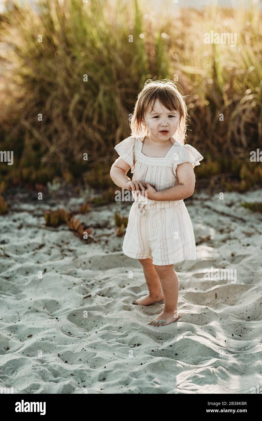 Pleine longueur de 2 ans, fille debout à la plage pendant le coucher du soleil Banque D'Images