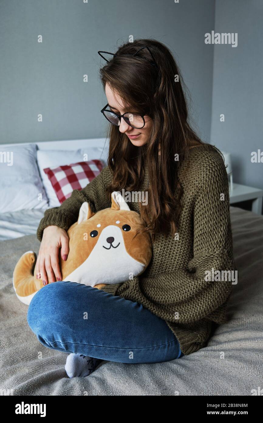 jeune fille à poil brun dans les oreilles de chat s'assoit sur un lit avec un jouet Banque D'Images
