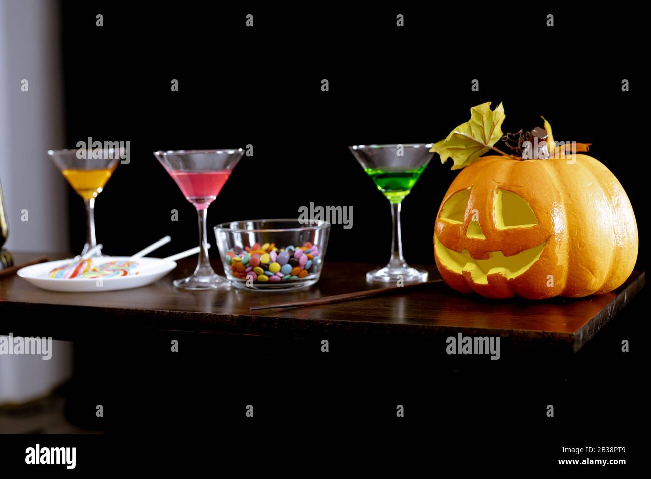 Citrouilles fantômes, bonbons et boissons sur la table à la fête d'Halloween dans la nuit sur fond sombre. Banque D'Images