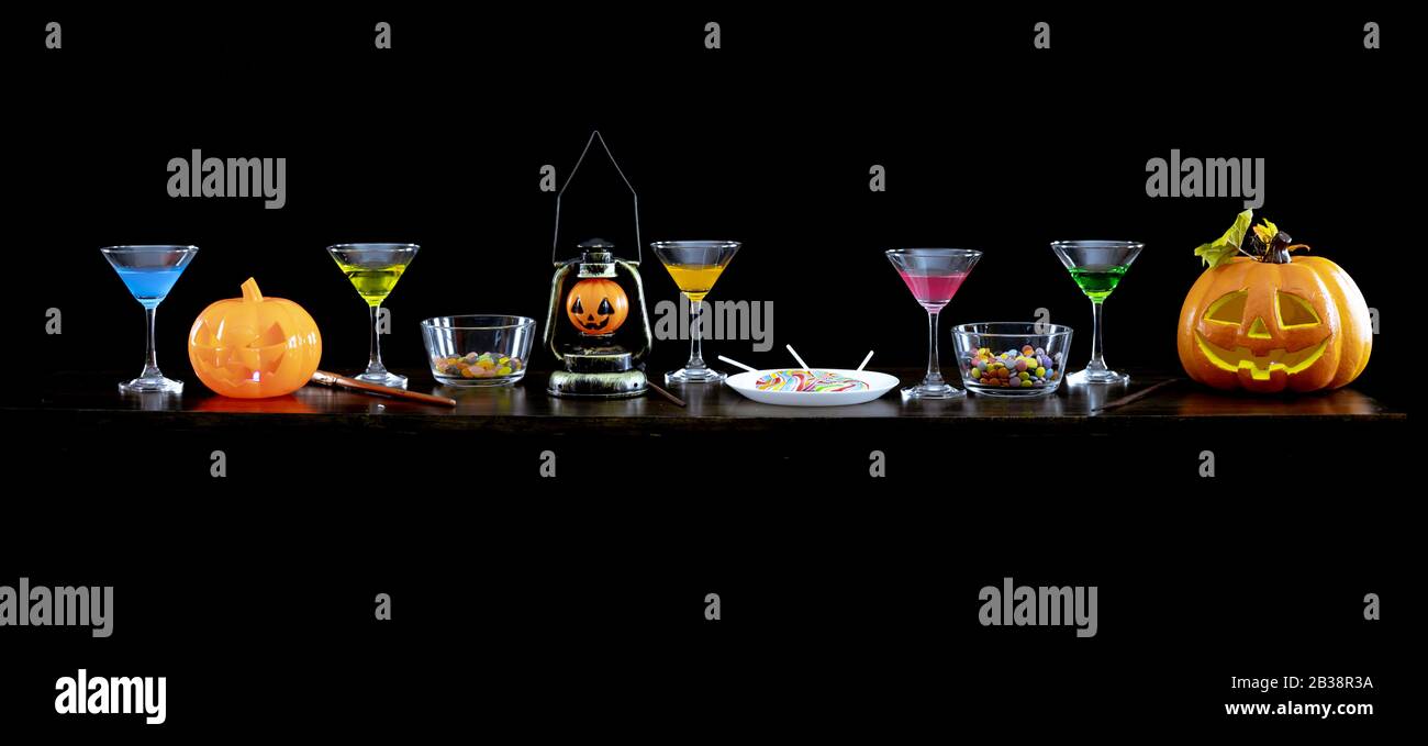 Citrouilles fantômes, bonbons et boissons sur la table à la fête d'Halloween dans la nuit sur fond sombre. Banque D'Images