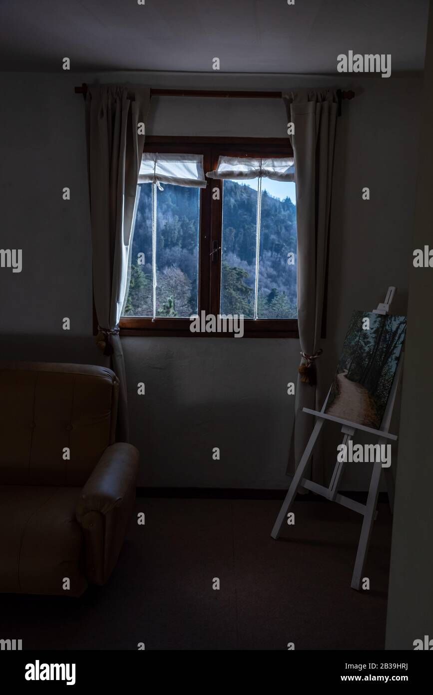 Regarder à travers une fenêtre une montagne pleine d'arbres. Sur le côté un fauteuil et une lanterne avec une peinture Banque D'Images