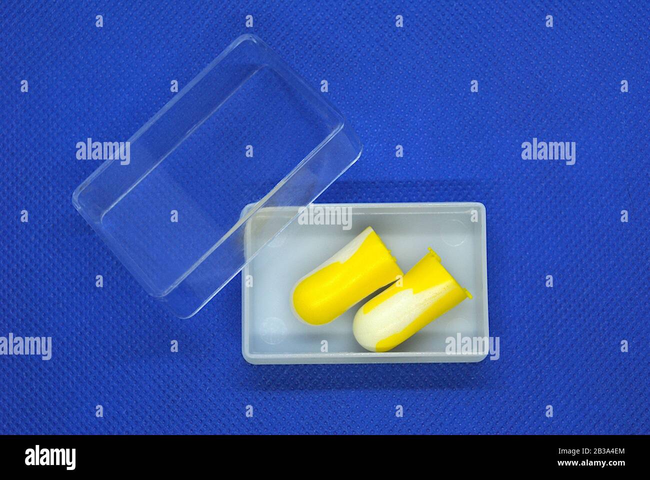 Paire isolée de bouchons d'oreilles colorés blancs et jaunes à l'intérieur d'un boîtier en plastique blanc avec couvercle transparent sur fond bleu Banque D'Images