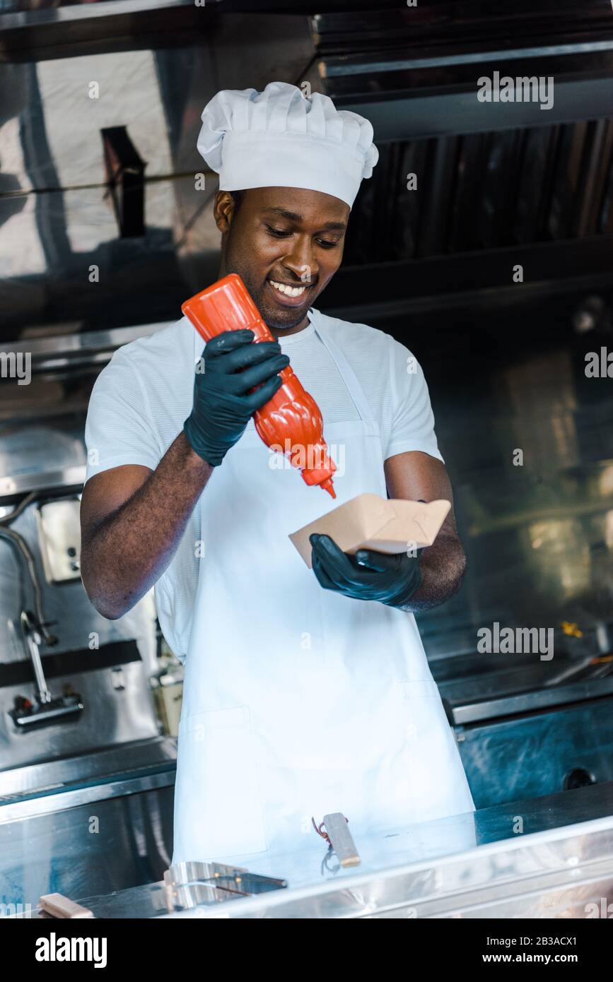 un homme afro-américain gai tenant une bouteille de ketchup près de la plaque de carton Banque D'Images