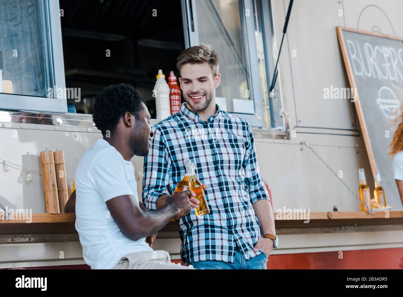des bouteilles de clinking pour hommes multiculturels et gaies avec de la bière près d'un camion alimentaire Banque D'Images