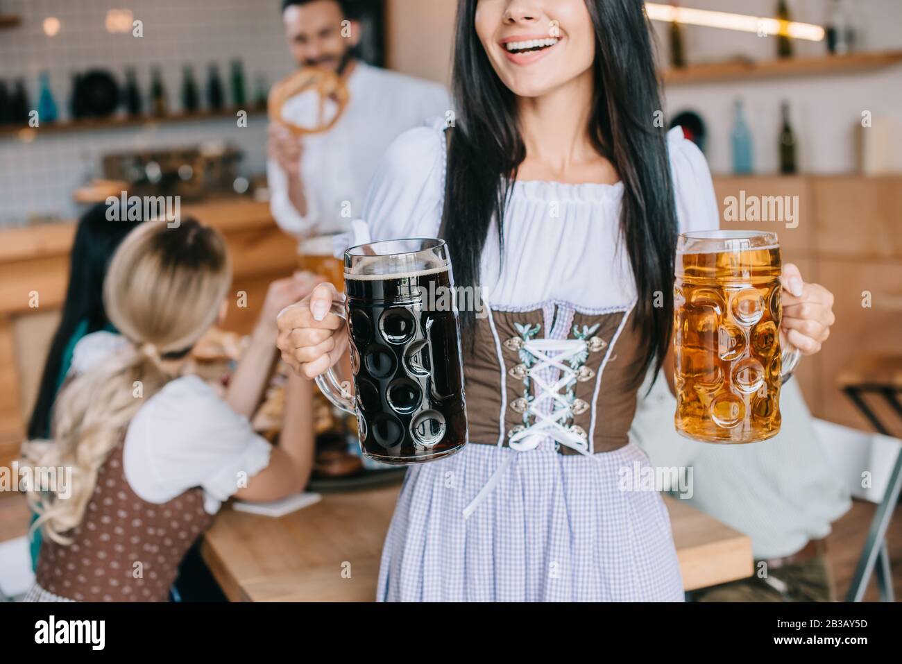 vue réduite de la serveuse dans un costume allemand traditionnel tenant des mugs de bière claire et sombre Banque D'Images