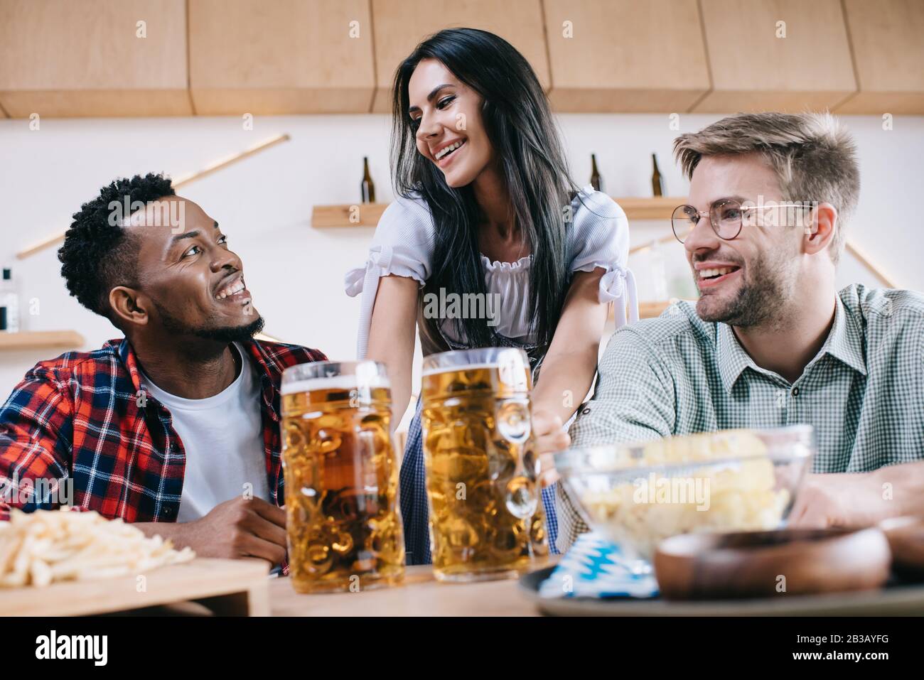 serveuse gaie en costume allemand traditionnel servant de la bière pour des amis multiculturels au pub Banque D'Images