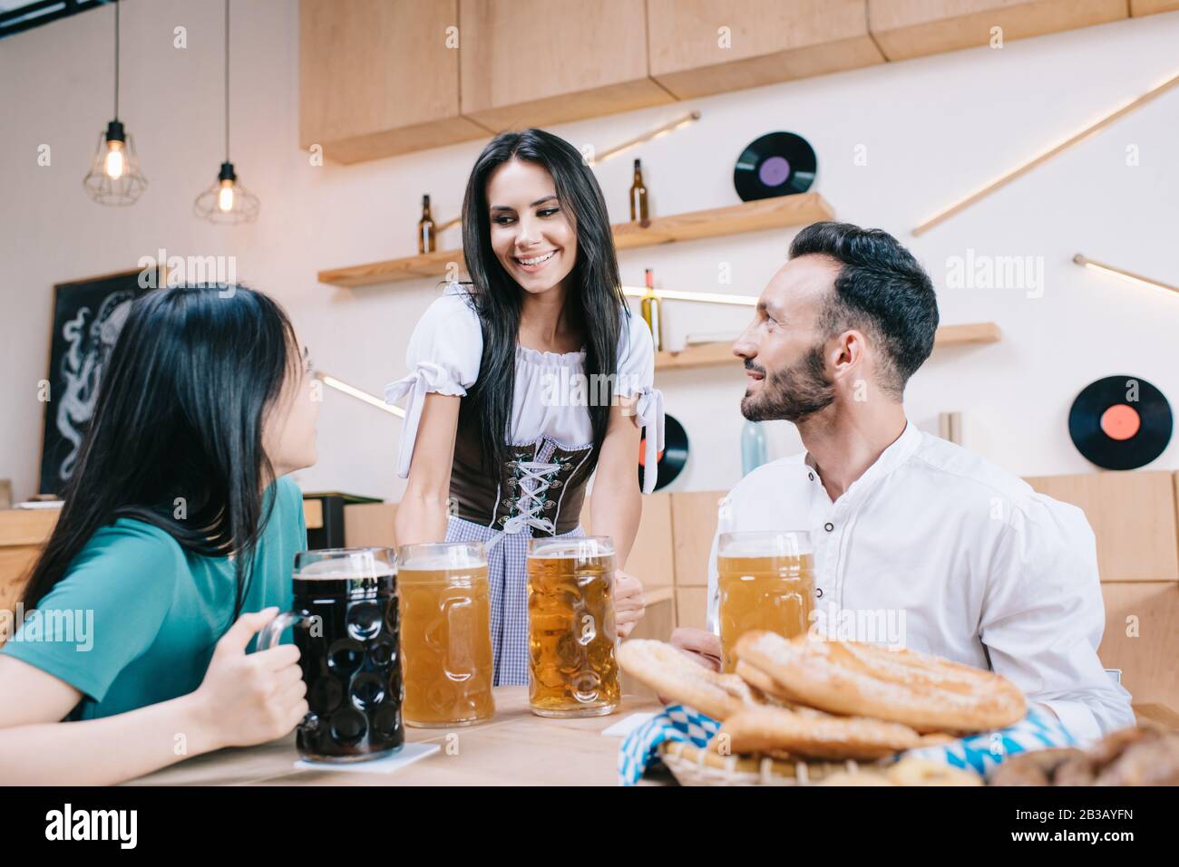 serveuse gaie en costume allemand traditionnel servant de la bière pour l'homme et la femme au pub Banque D'Images