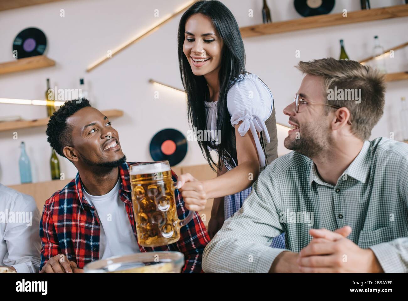 belle serveuse en costume allemand traditionnel servant de la bière pour des amis multiculturels au pub Banque D'Images