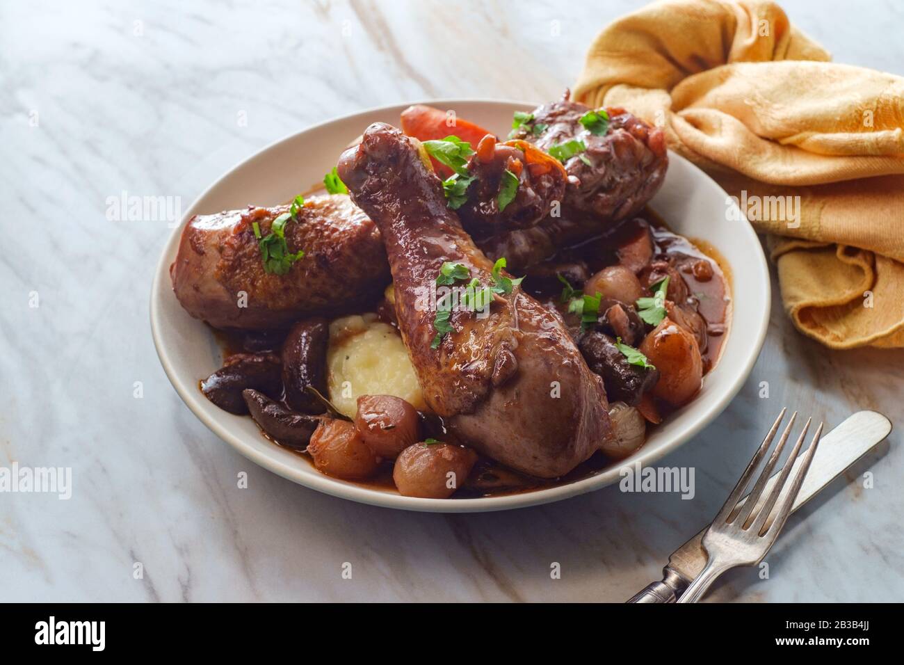 Cuisine française Coq au vin ragoût avec des champignons crimini oignons perlés et carottes dans une sauce au brandy au vin rouge servie sur une purée de pommes de terre Banque D'Images