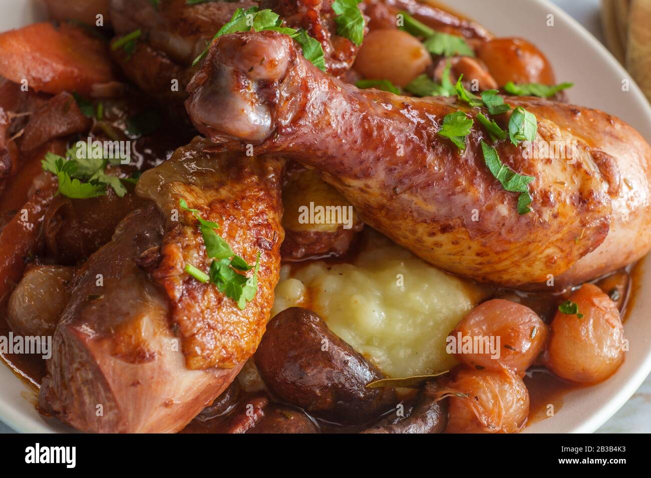 Cuisine française Coq au vin ragoût avec des champignons crimini oignons perlés et carottes dans une sauce au brandy au vin rouge servie sur une purée de pommes de terre Banque D'Images