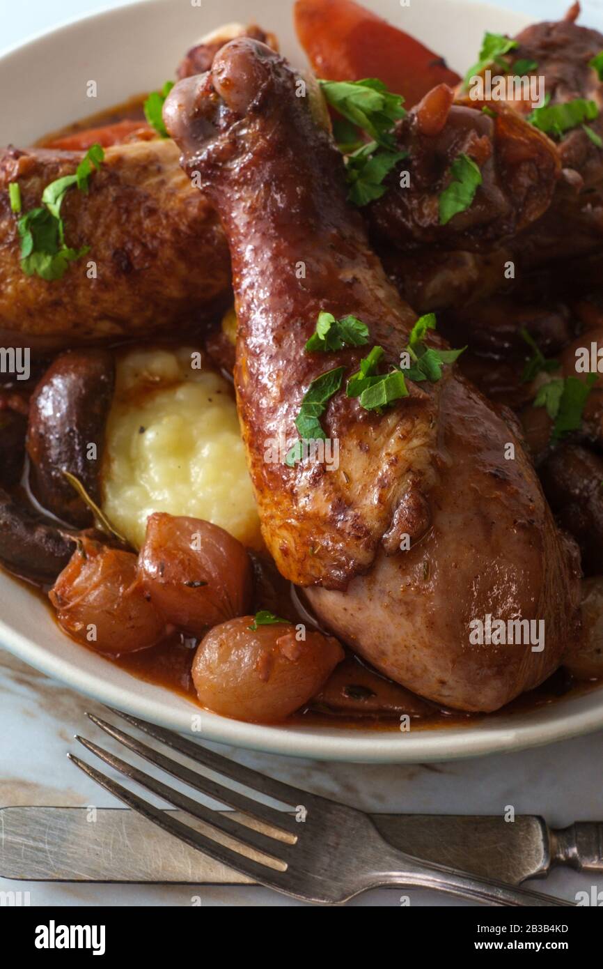 Cuisine française Coq au vin ragoût avec des champignons crimini oignons perlés et carottes dans une sauce au brandy au vin rouge servie sur une purée de pommes de terre Banque D'Images