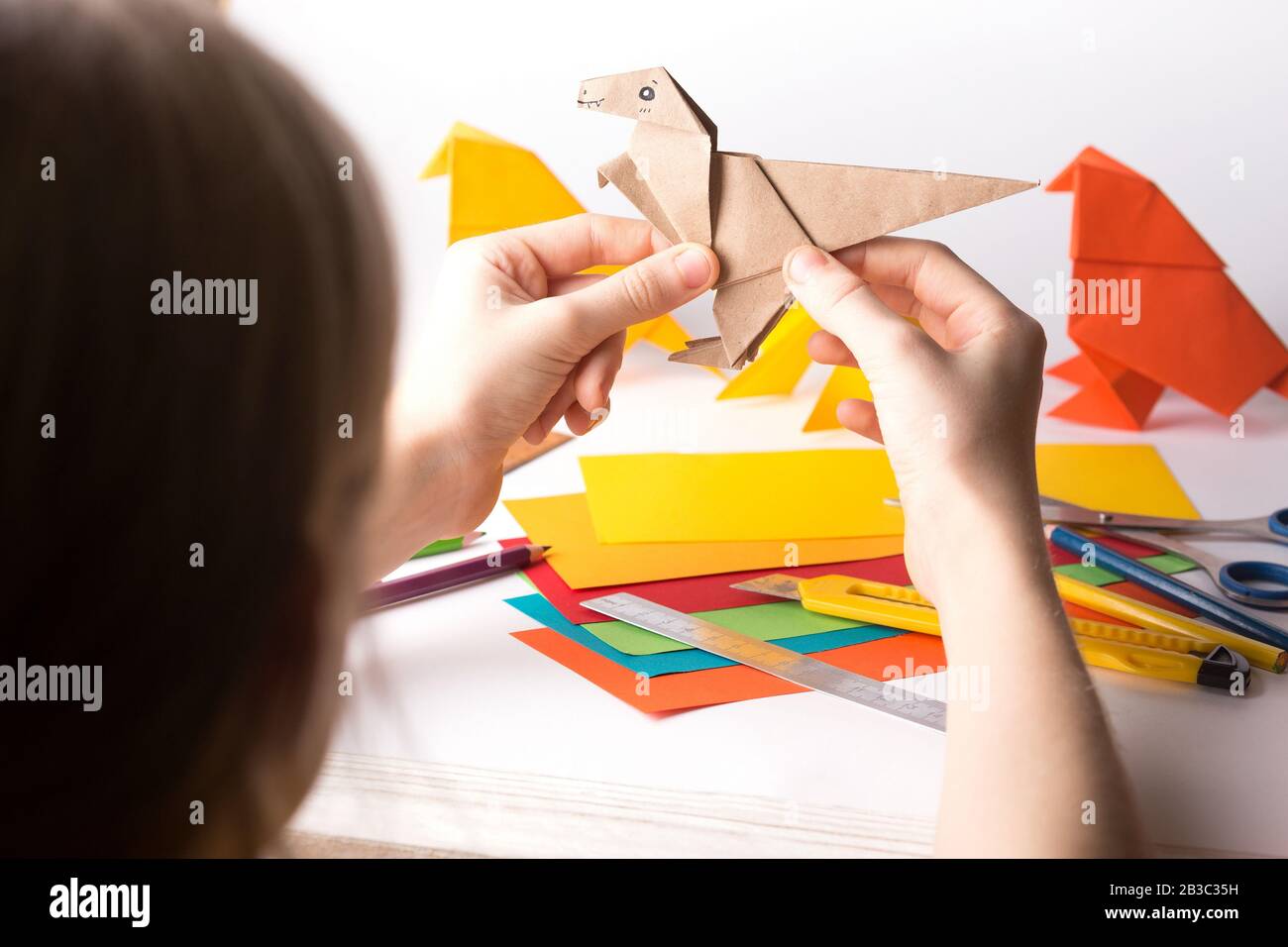 fille fait origami dinosaure de papier de couleur. papier, règle, crayons, couteau. passe-temps intéressant Banque D'Images
