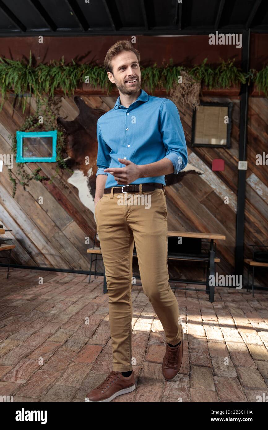 Homme confiant et décontracté expliquant et gestant tout en portant une  chemise bleue et un pantalon marron, marchant sur un fond de café Photo  Stock - Alamy
