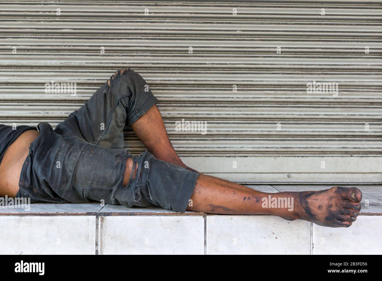 Un pauvre sans-abri ou un réfugié dormant sur le banc en bois de la rue urbaine de la ville. Banque D'Images