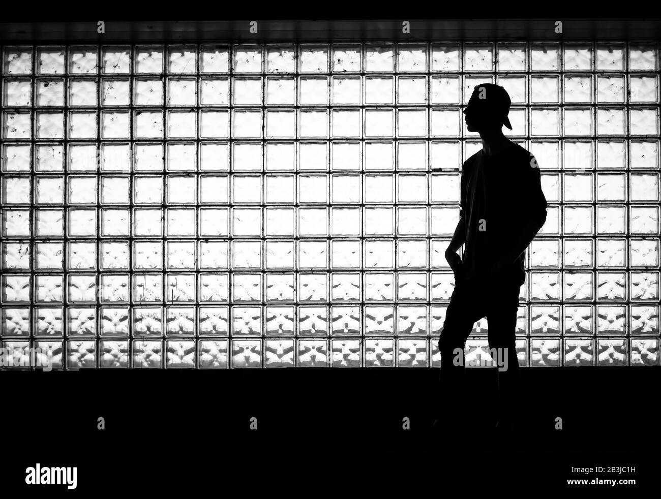 Silhouette d'un jeune homme debout contre le mur de carreaux de verre, illuminé par le soleil. Coup de clé faible Banque D'Images