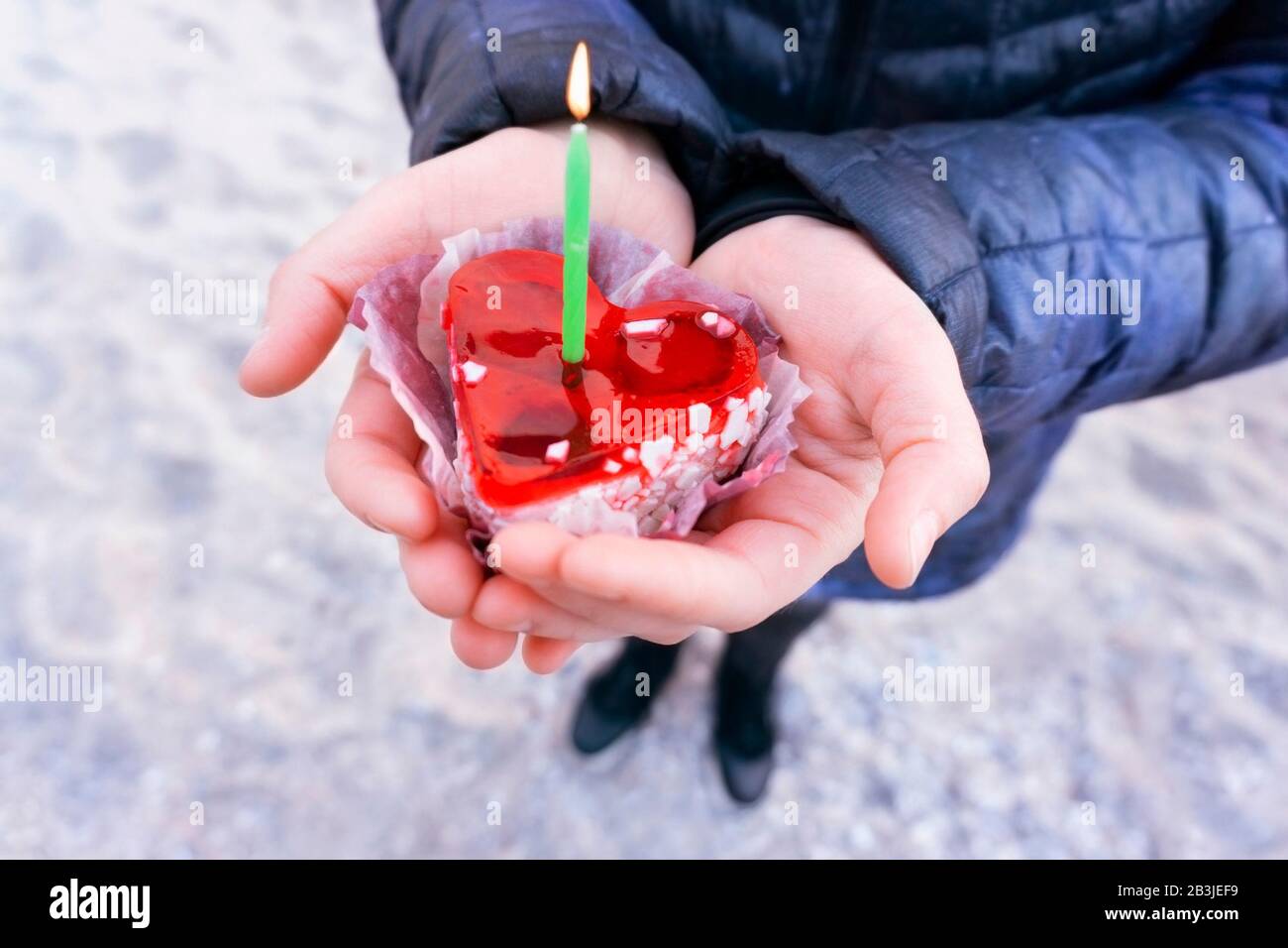 Les mains des femmes tiennent un gâteau en forme de coeur avec une bougie Banque D'Images