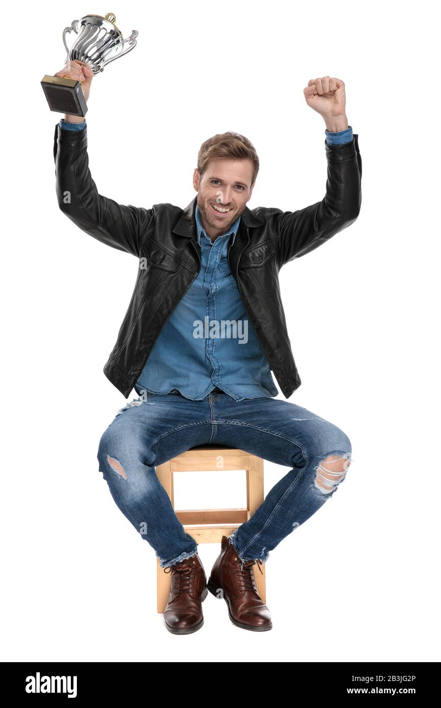bel homme décontracté avec veste en cuir noir est assis sur une chaise en bois tenant ses mains dans l'air avec sa tasse enchantée sur le studio blanc bac Banque D'Images