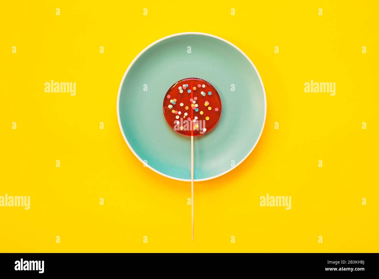 Un grand Lollipop rouge sur la plaque bleue, sur un fond jaune. Concept minimal. Banque D'Images