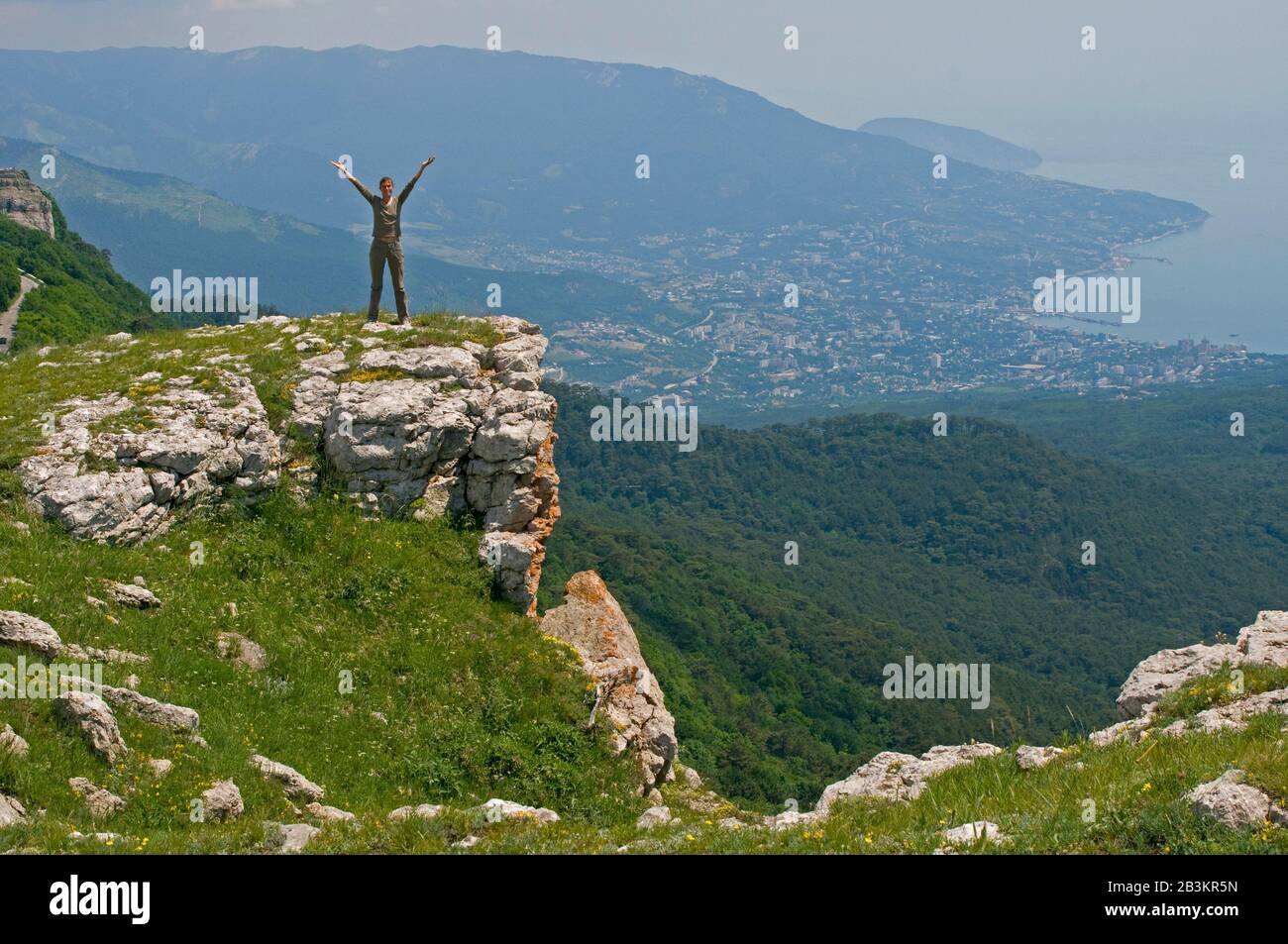 La jeune femme se tient au bord d'Ay-Petri Yayla (dans les montagnes de Crimée). La ville de Yalta, le mont Ayu-Dag et la mer sont en arrière-plan. Banque D'Images