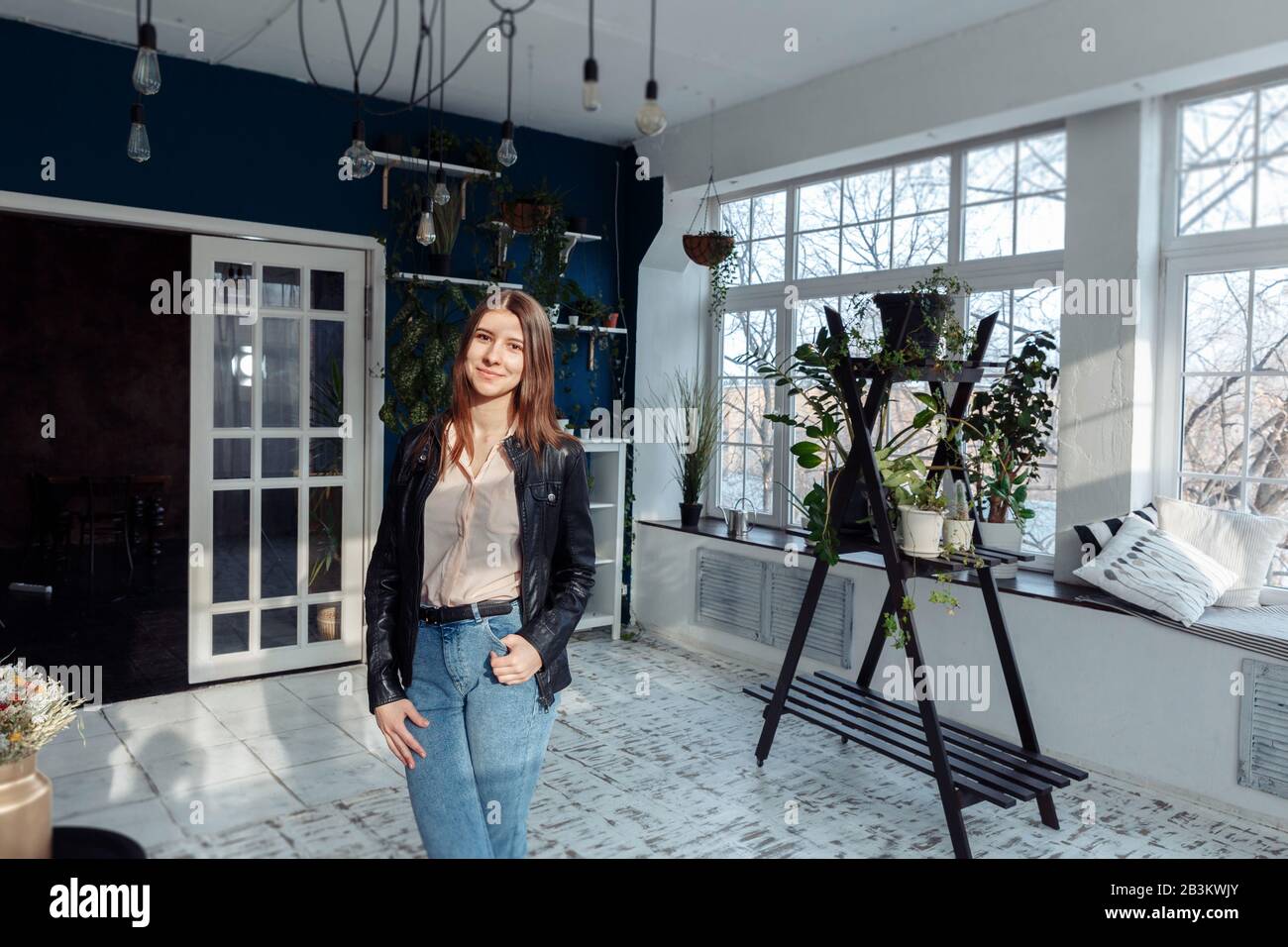 Une fille dans une veste en cuir stot au milieu d'une chambre lumineuse. La chambre a des plantes à la maison. Banque D'Images