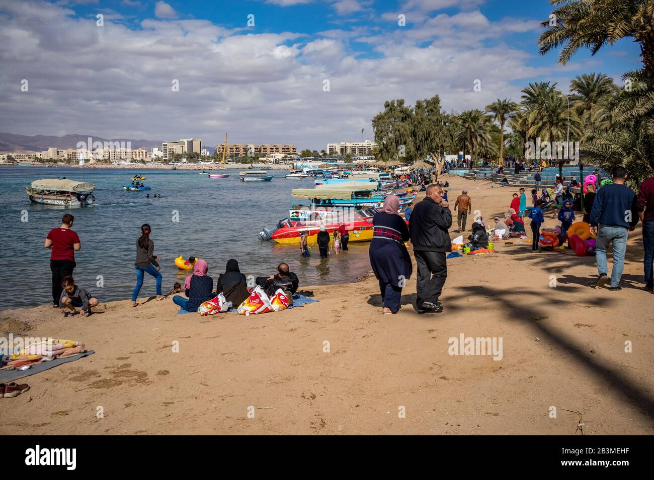 Aqaba, JORDANIE - 31 JANVIER 2020: Les gens et les touristes locaux profitent de vacances vendredi à la plage ensoleillée de la ville avec des bateaux de plancher de verre. Hiver nuages puffy ciel du matin. golfe de la Mer Rouge, Royaume hachémite de Jordanie Banque D'Images