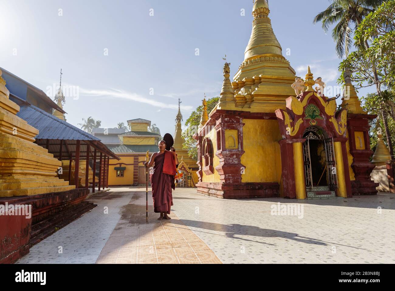 Un moine dans des robes de salon tenant un personnel et un bol en acier d'alms debout dans le domaine d'un temple, Sittwe, Rakhine, Myanmar (Birmanie), Asie Banque D'Images