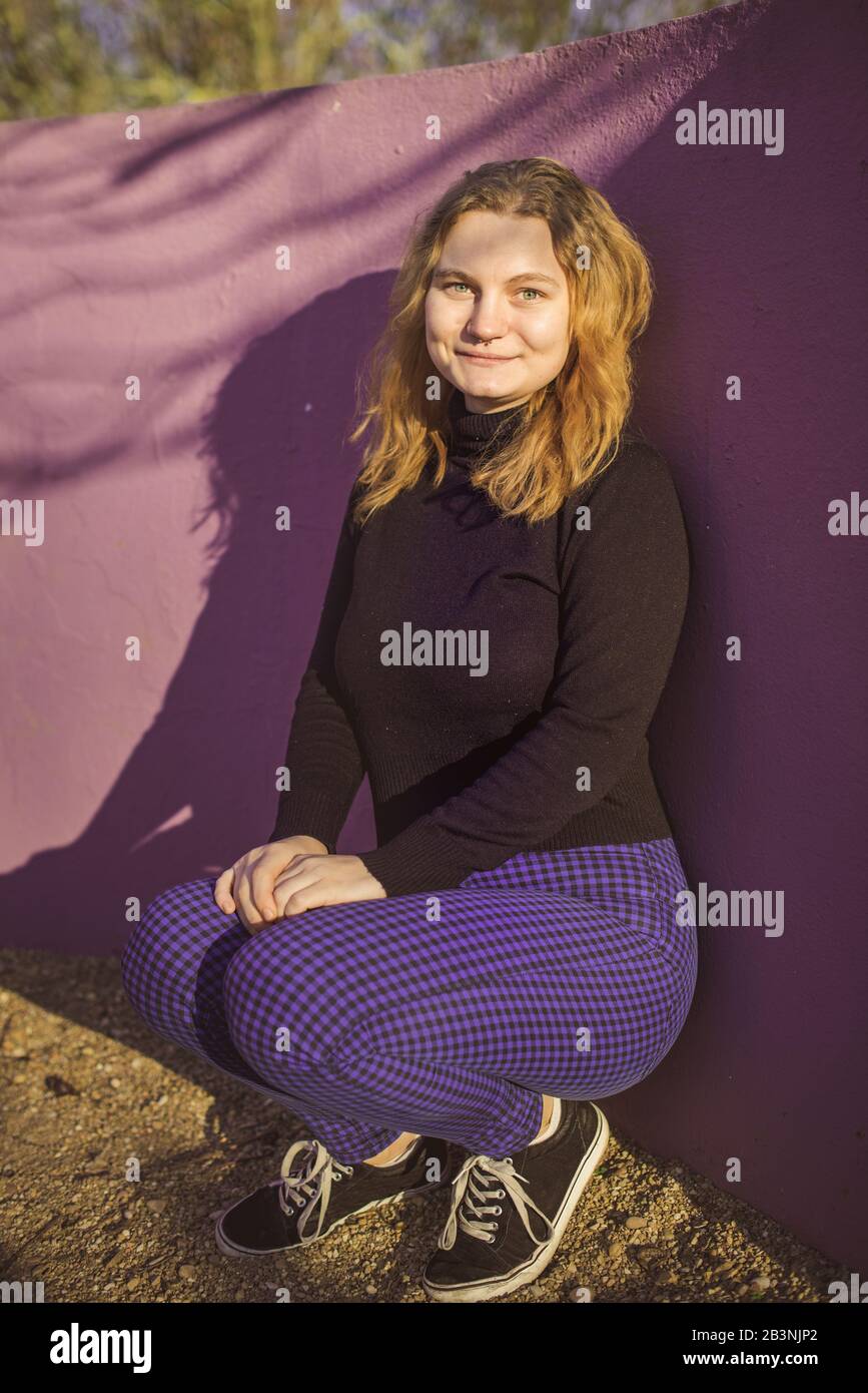 blonde fille aux yeux bleus avec mur violet comme arrière-plan dans un parc en hiver ensoleillé après-midi Banque D'Images