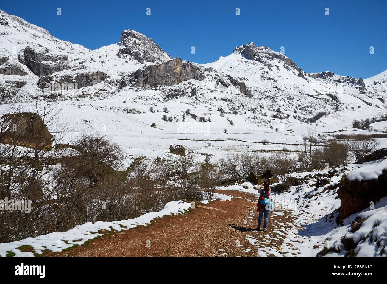 Randonneur féminin en PR.AS-15 chemin de randonnée avec teitos et montagnes enneigées en arrière-plan (Valle del Lago, Soriedo Natural Park, Asturies, Espagne) Banque D'Images