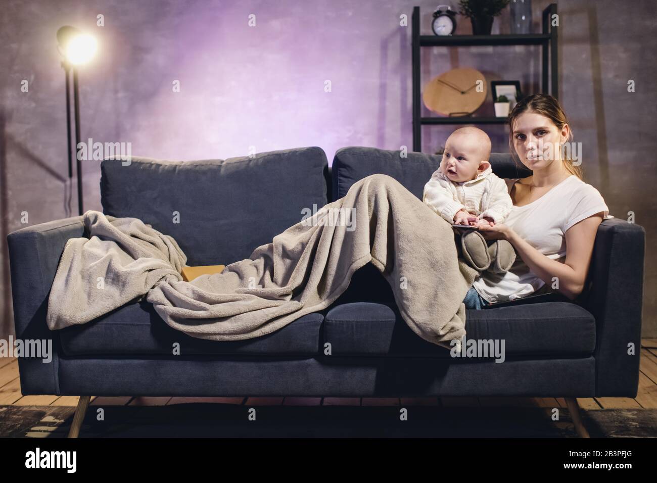 Une Jeune Fille Avec Un Enfant Regardant La Television Maman Et Bebe Sont Allonge Sur Le Canape Chambre Confortable Photo Stock Alamy