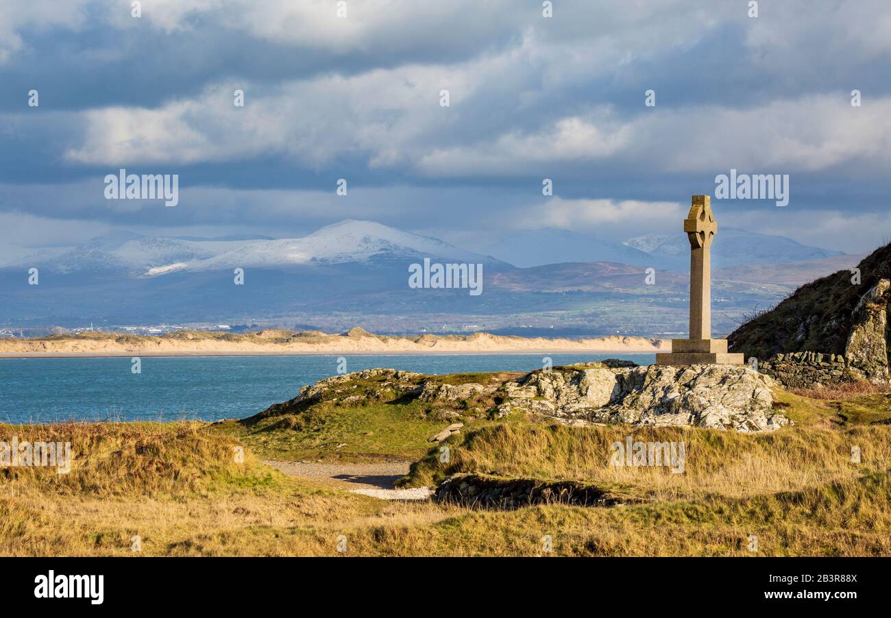 La croix celtique sur l'île de Llanddwyn avec les dunes de sable de la plage de Newborough et les montagnes enneigées de Snowdonia en arrière-plan, Anglesey Banque D'Images