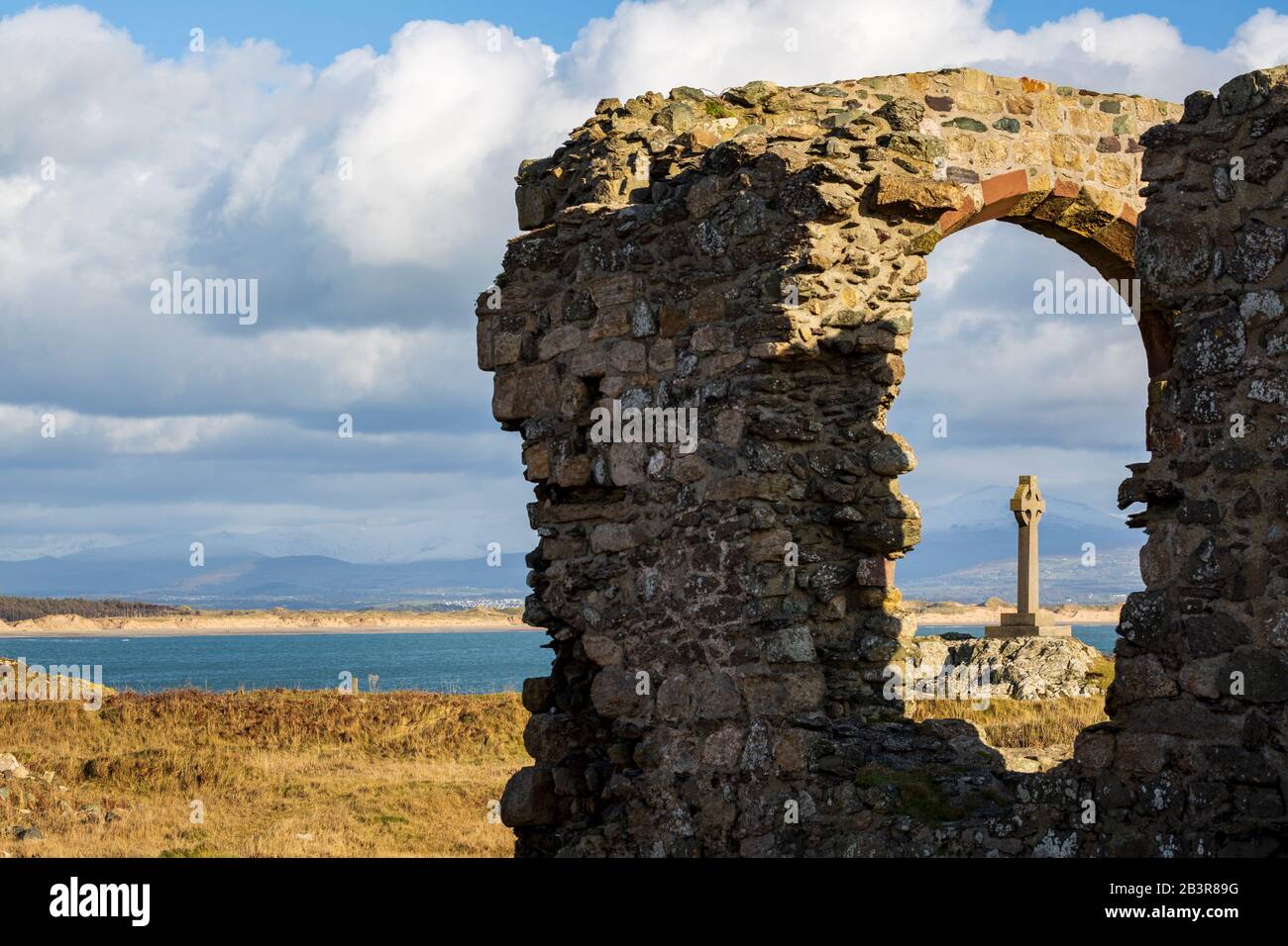 La croix celtique a vu à travers les ruines de l'église de St Dwynwen sur l'île de Llanddwyn, Anglesey Banque D'Images